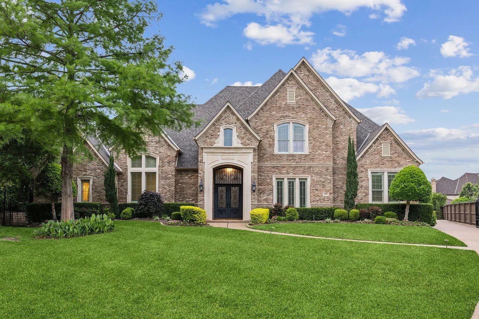 Large brick house with manicured lawn, trees, and a clear blue sky background.
