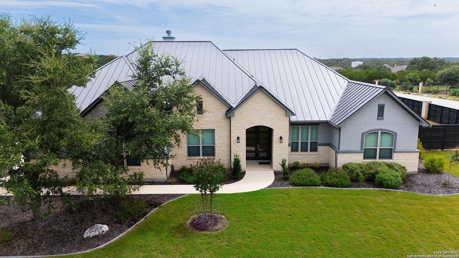 Single-story house with a metal roof, surrounded by trees and a well-maintained lawn.