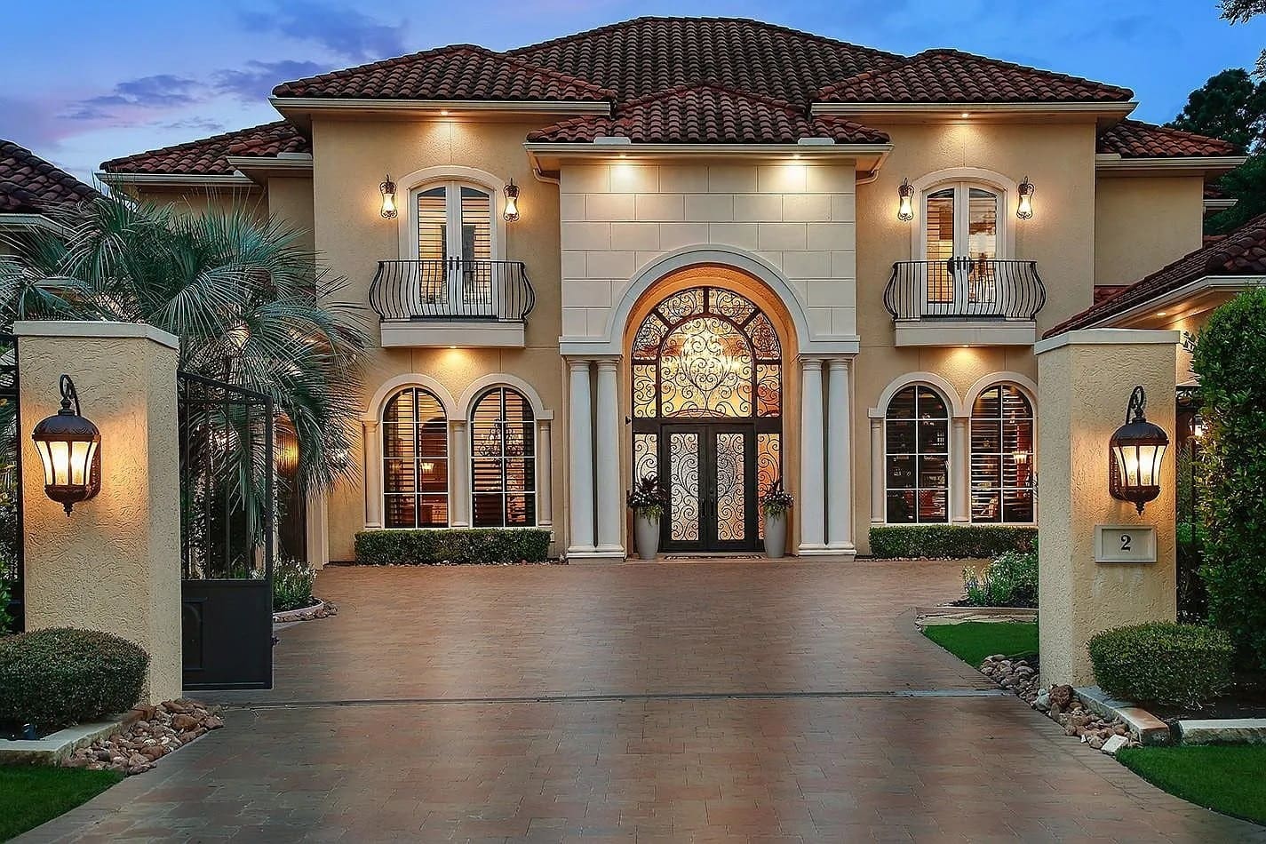 Elegant two-story house with arched entrance, ornate doors, and warm exterior lighting at dusk.
