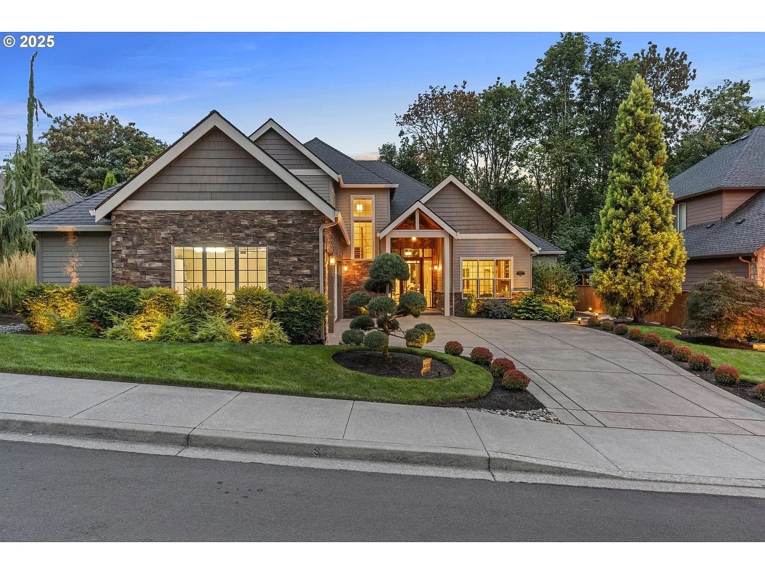 Modern suburban house with stone and wood exterior, landscaped front yard, and evening lighting.
