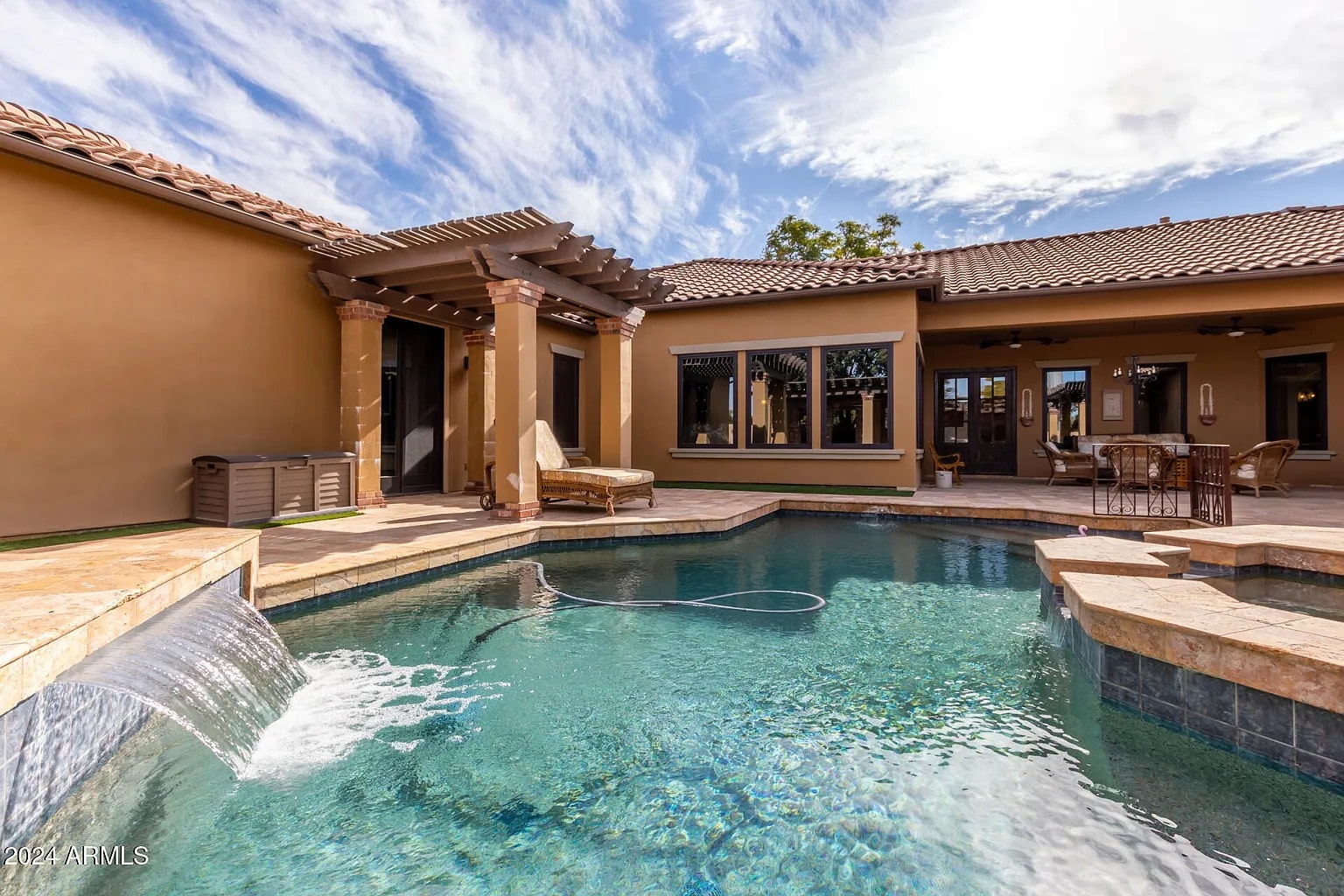 Backyard view of a luxurious house with a swimming pool and waterfall feature.