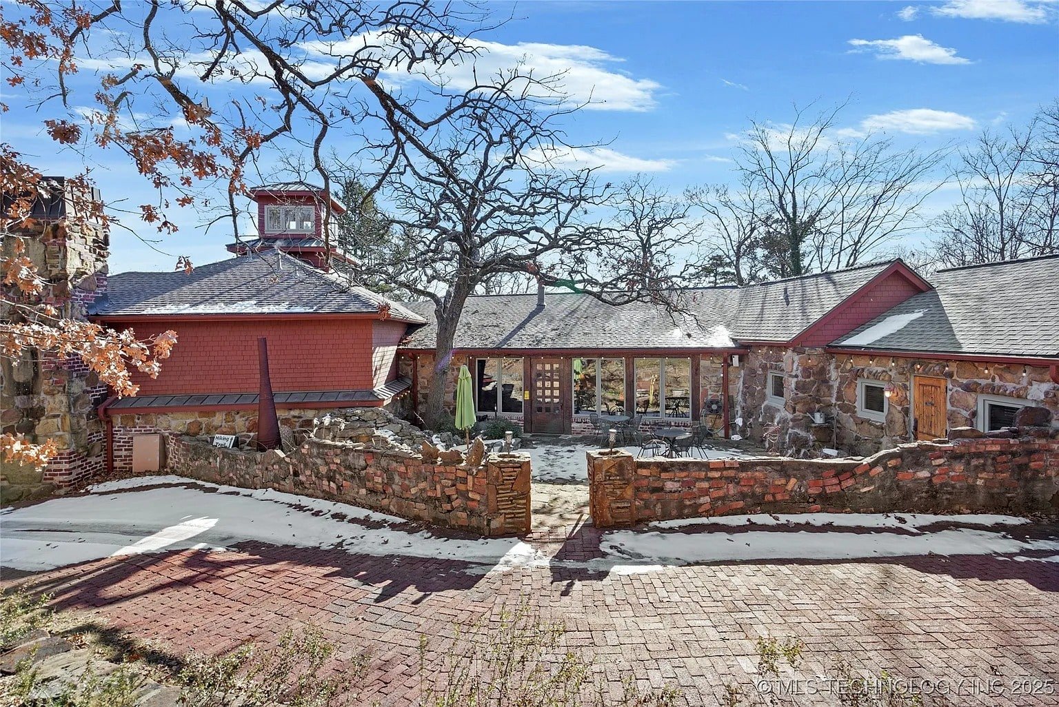 Historic stone and brick house with a courtyard, surrounded by trees and a clear blue sky.