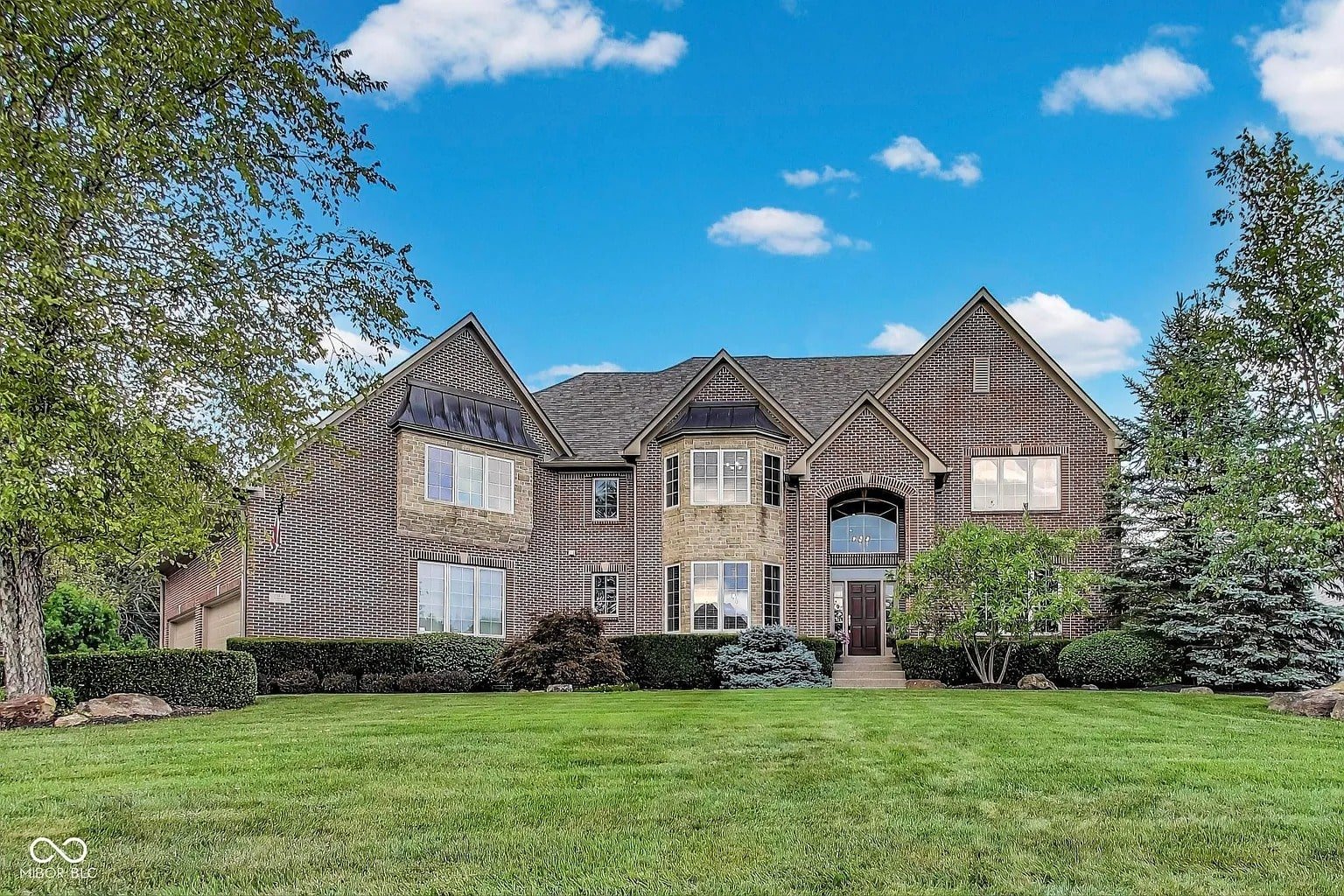 Large brick house with a well-maintained lawn and clear blue sky.