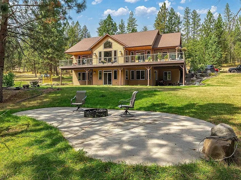 Large two-story house with a spacious balcony, surrounded by trees, and a patio with chairs.