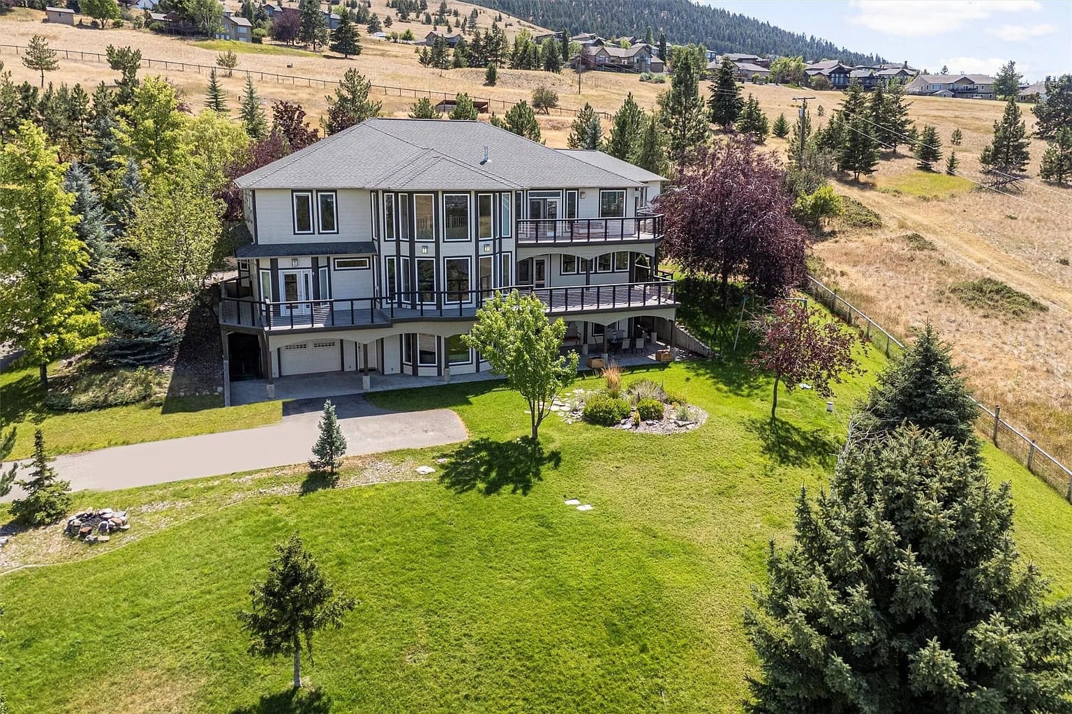 Large two-story house with wraparound balconies, surrounded by trees and a grassy landscape.