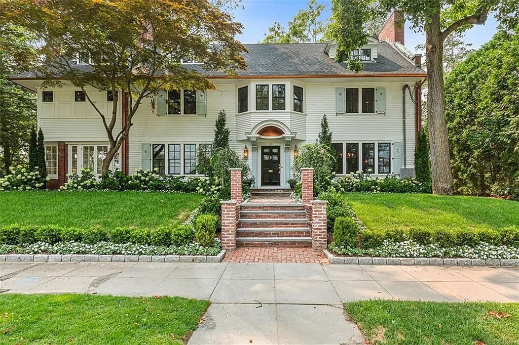 Large two-story white house with brick steps, surrounded by green lawn and trees.