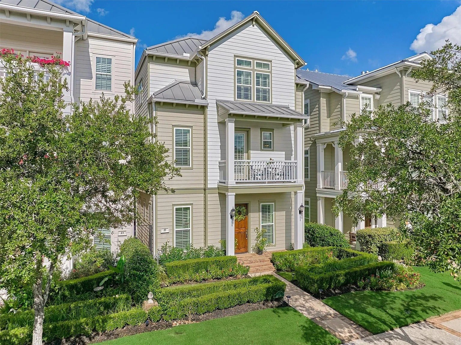 Three-story white house with a small front porch, surrounded by trees and manicured bushes.