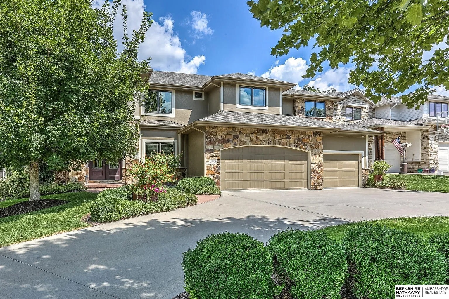 Two-story suburban house with a three-car garage, surrounded by trees and shrubs.