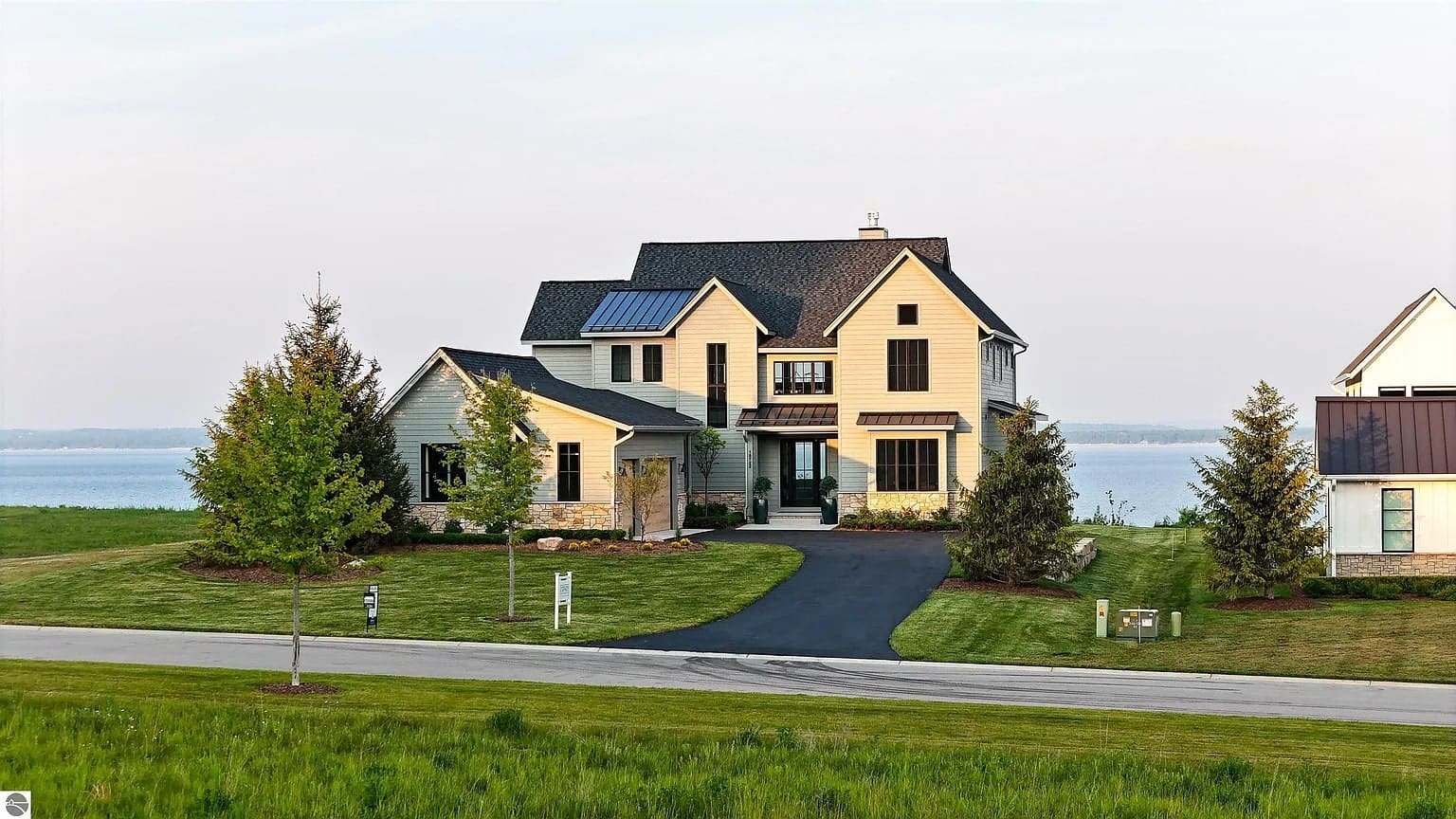 Two-story house with a large driveway, surrounded by trees and a lake in the background.