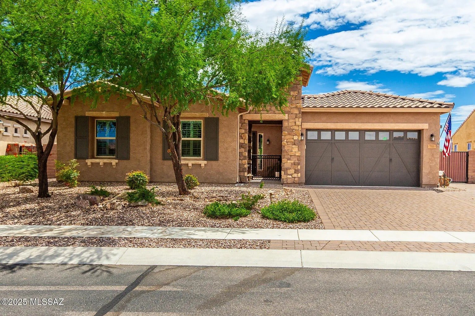 Single-story house with stone accents, two-car garage, and landscaped front yard under a blue sky.