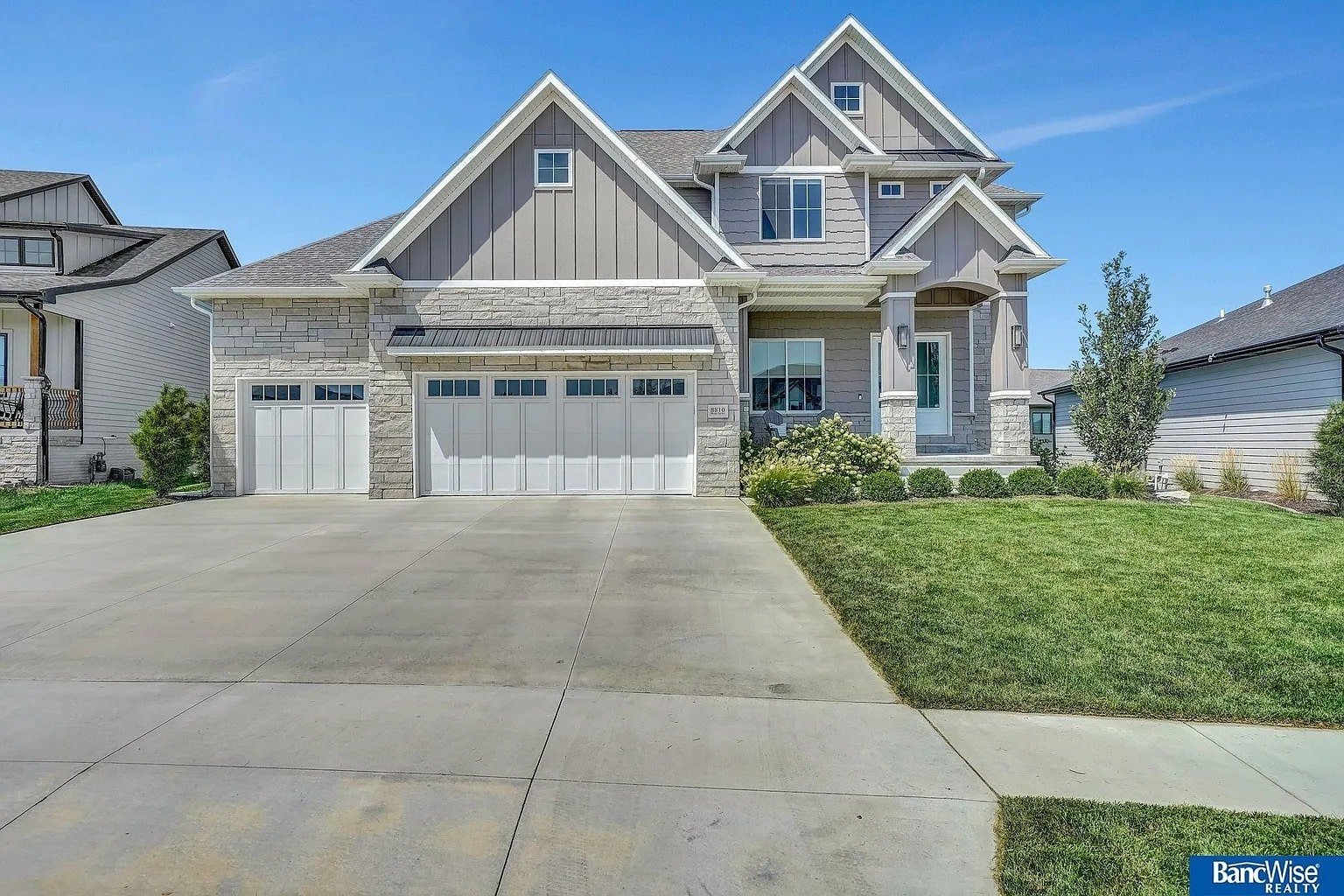 Modern two-story house with a three-car garage and well-maintained lawn on a sunny day.