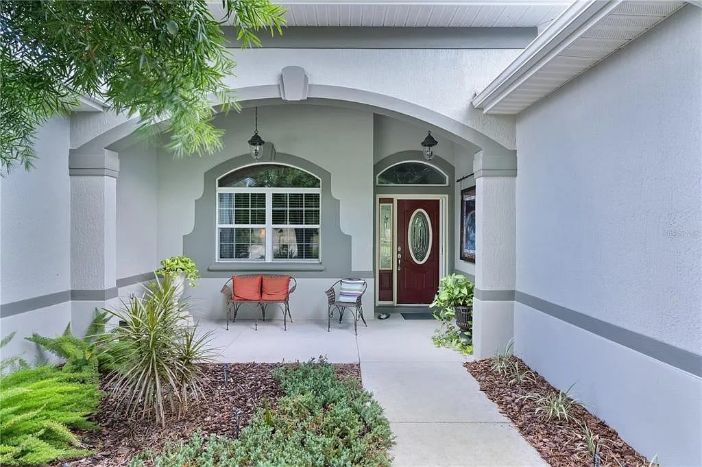 Front porch with arched entryway, red door, bench, and plants on either side.