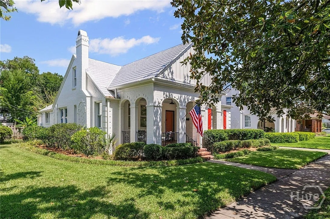 White house with a manicured lawn, American flag, and a tree-lined sidewalk.