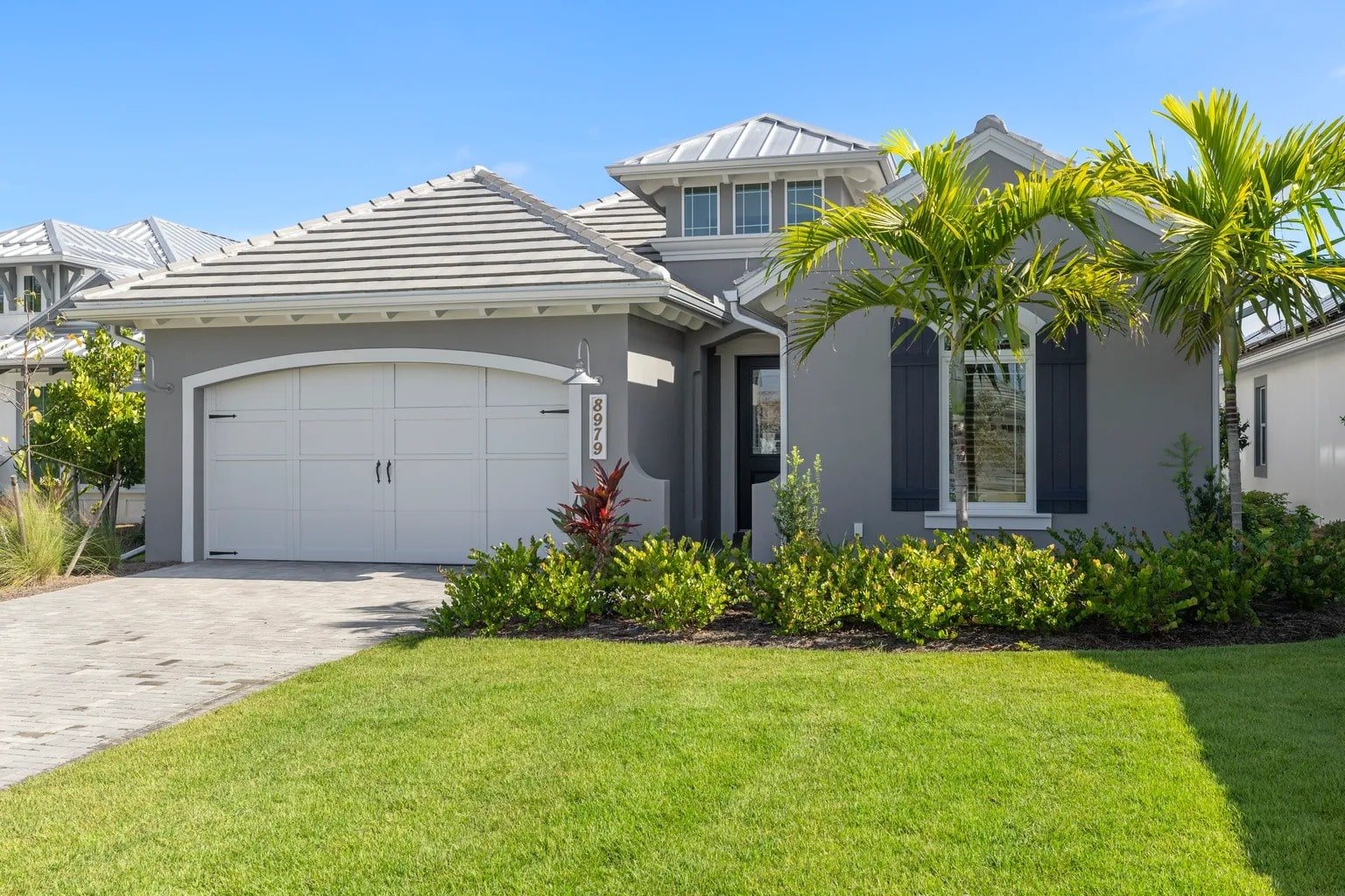 Modern gray house with a two-car garage, palm trees, and a well-maintained lawn.