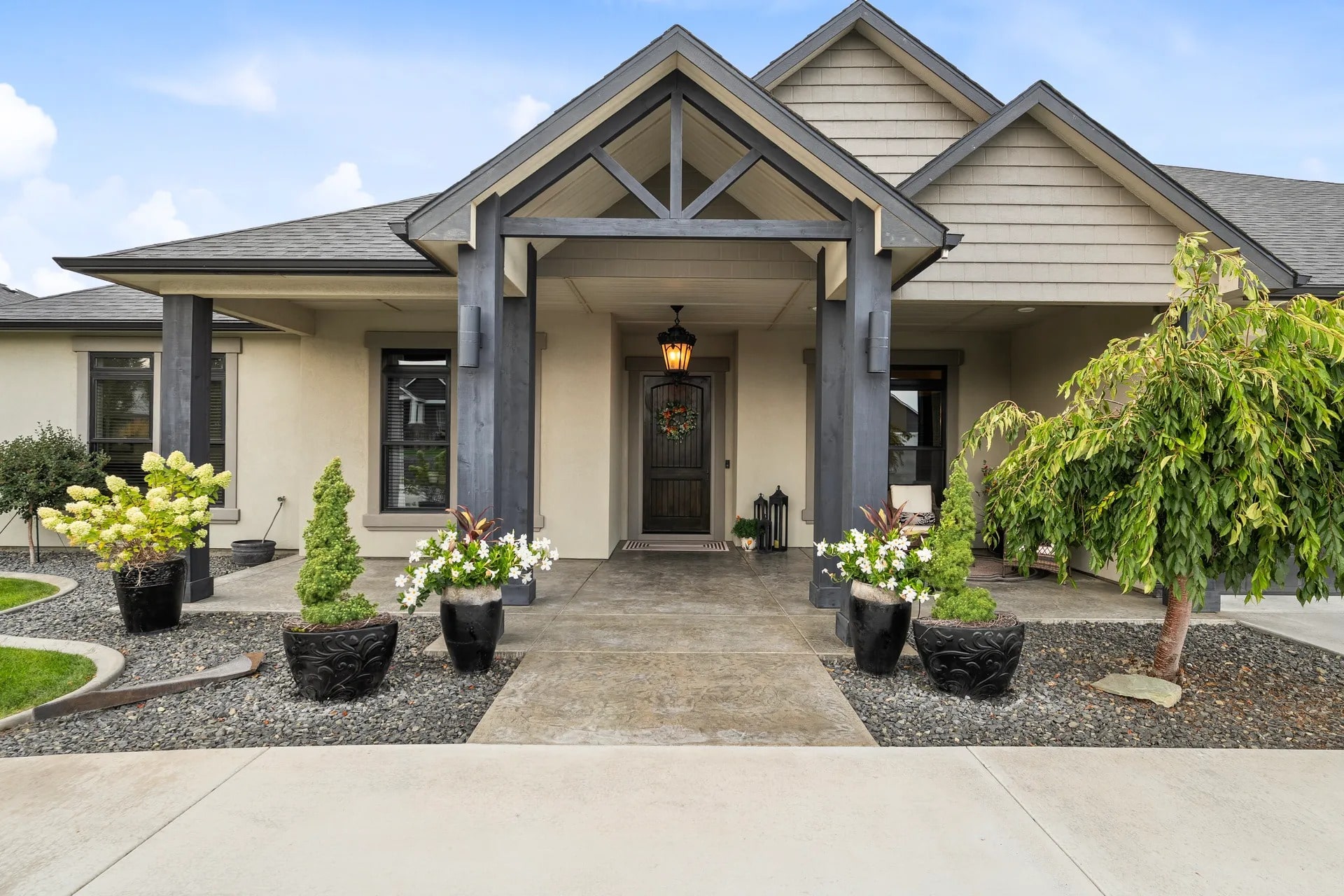 Modern house entrance with a covered porch, decorative plants, and a central wooden door.