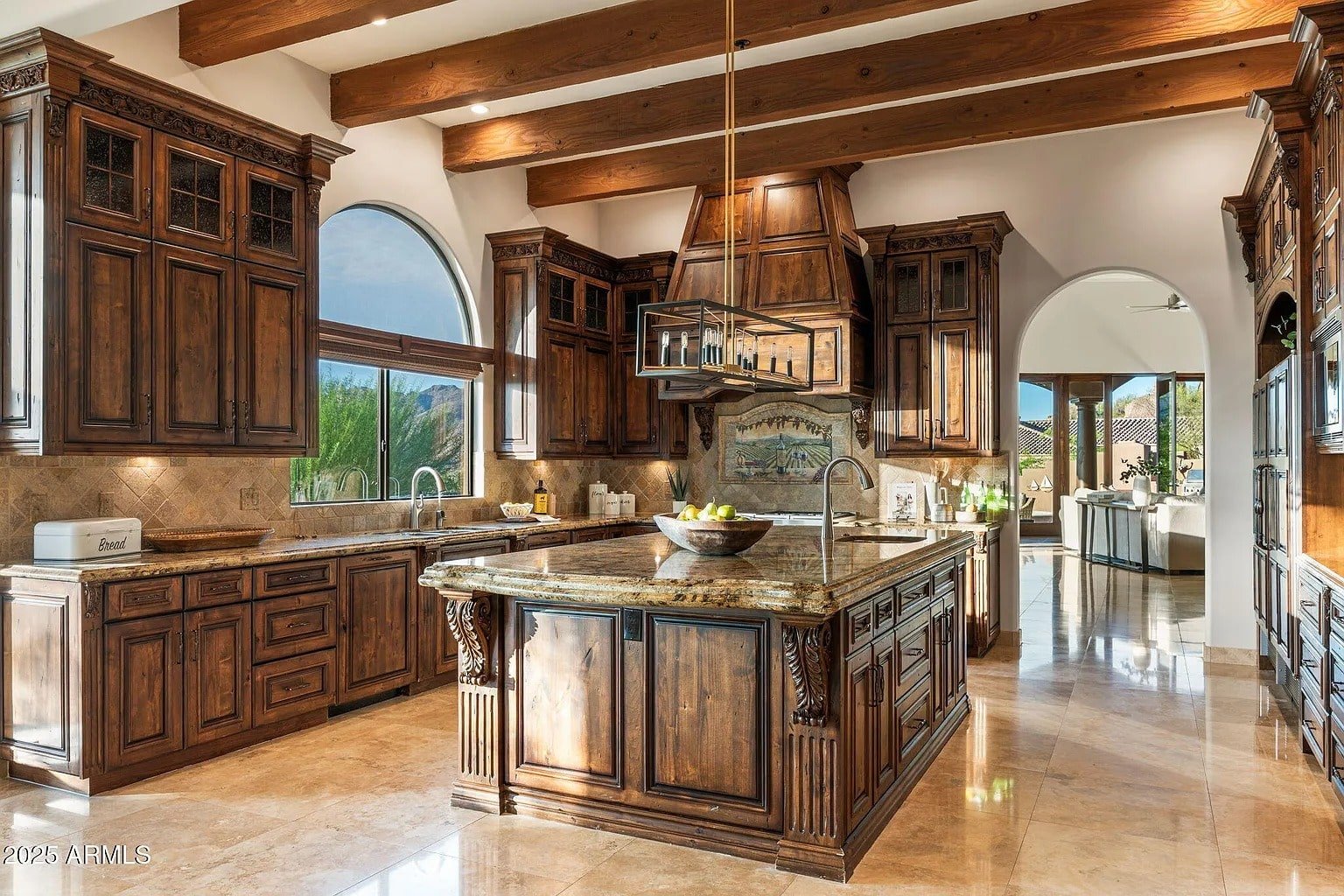 Spacious kitchen with wooden cabinets, large island, and arched windows overlooking a scenic view.