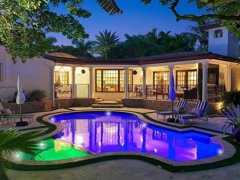 A luxurious villa with a lit swimming pool, surrounded by trees, at dusk.