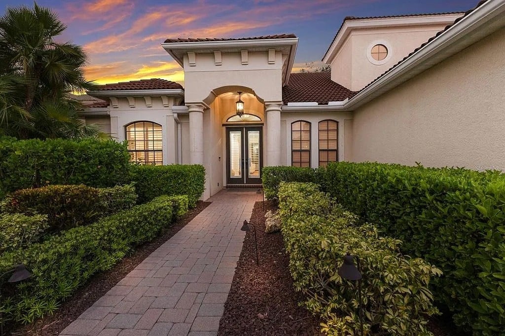 Pathway leading to a modern house entrance, surrounded by manicured hedges, at sunset.