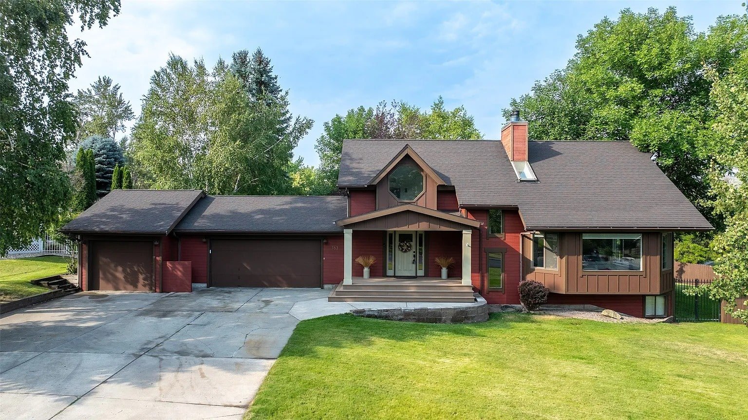 A modern, two-story house with a large driveway and surrounding greenery.