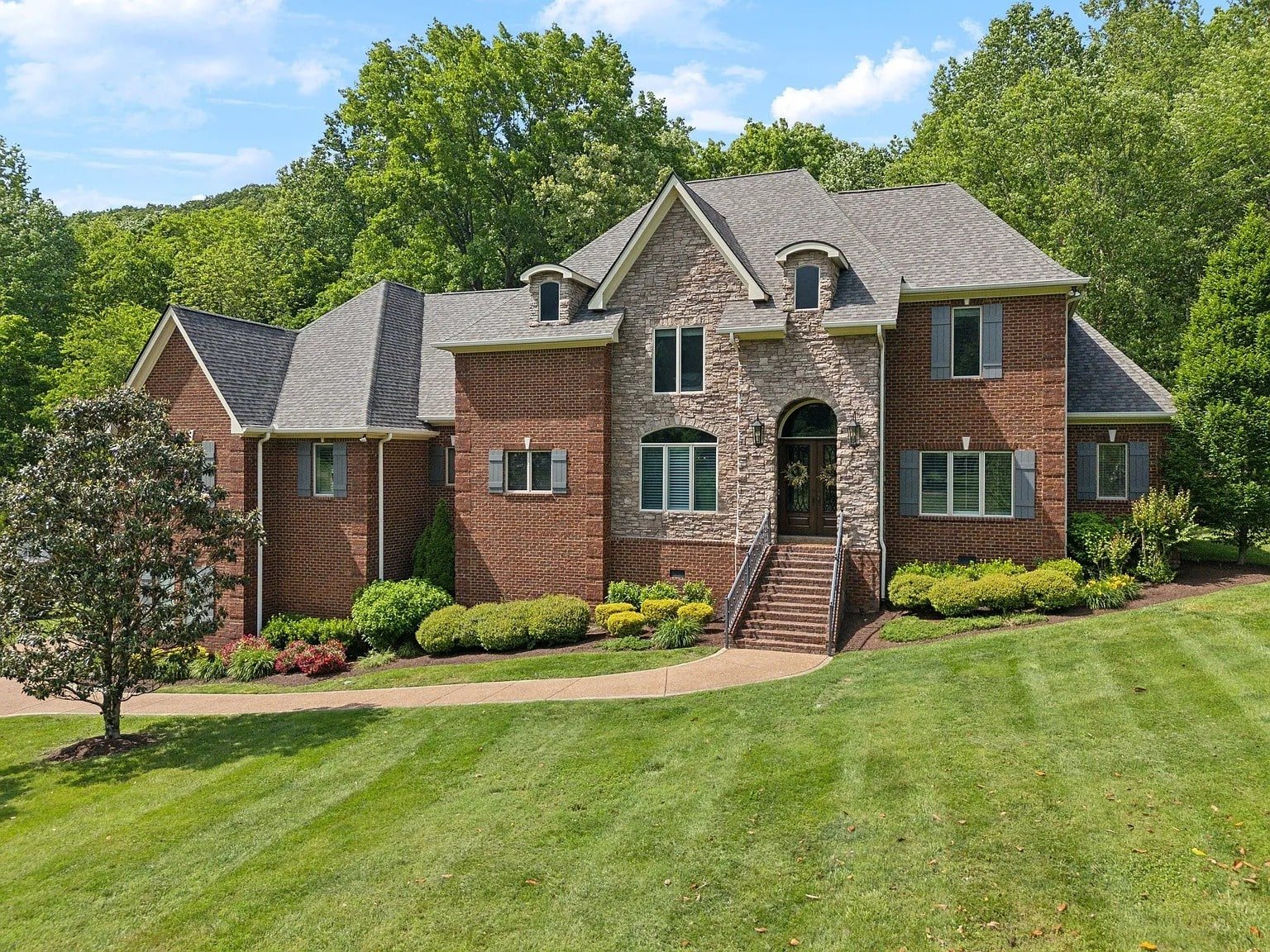 Large brick house with a manicured lawn, surrounded by trees under a clear blue sky.
