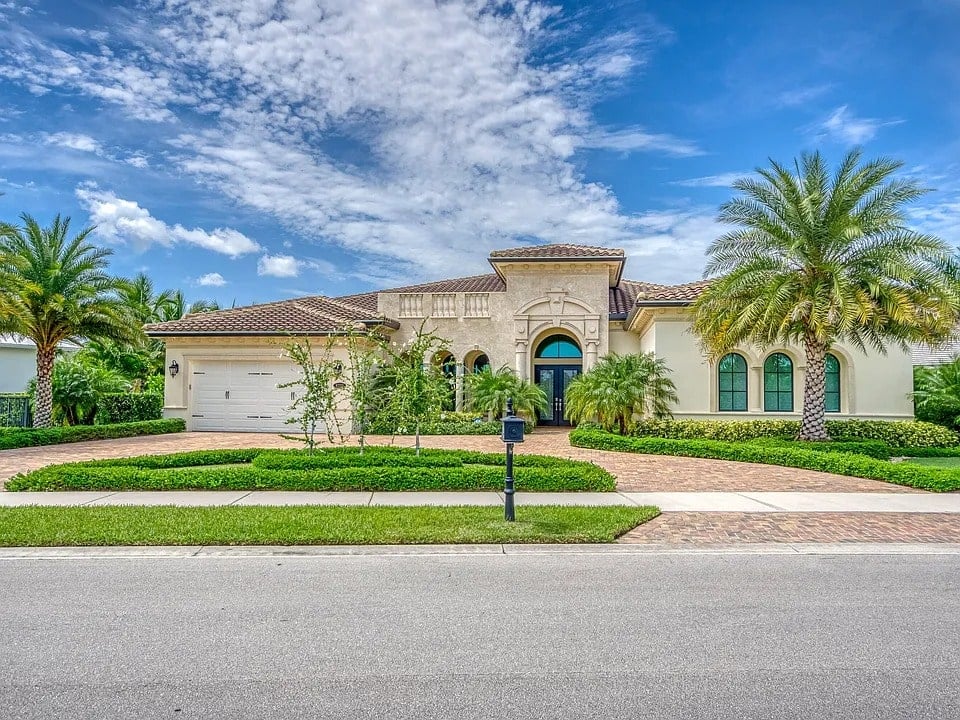 Single-story Mediterranean-style house with palm trees, arched windows, and a brick driveway.