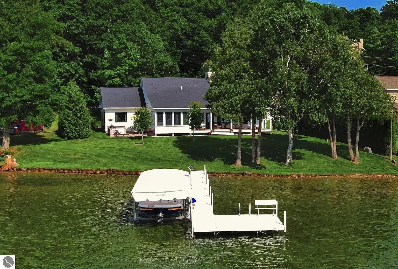 House with a dock and boat on a lake, surrounded by trees and greenery.