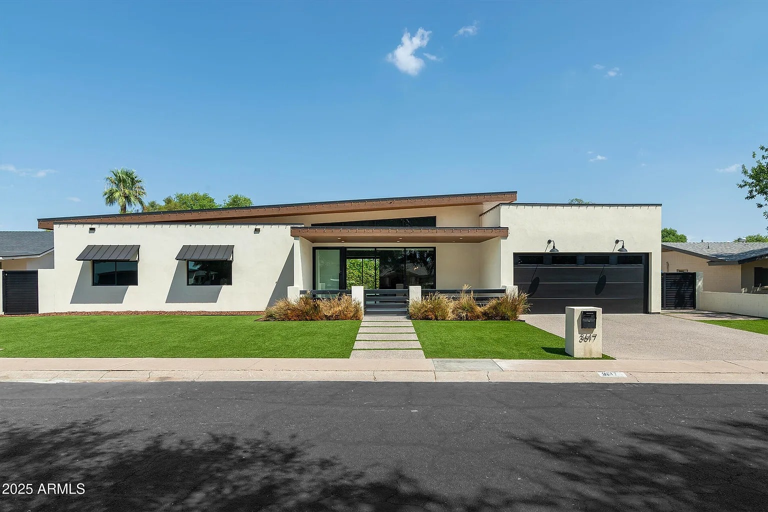Modern single-story house with flat roof, large windows, and a manicured lawn.