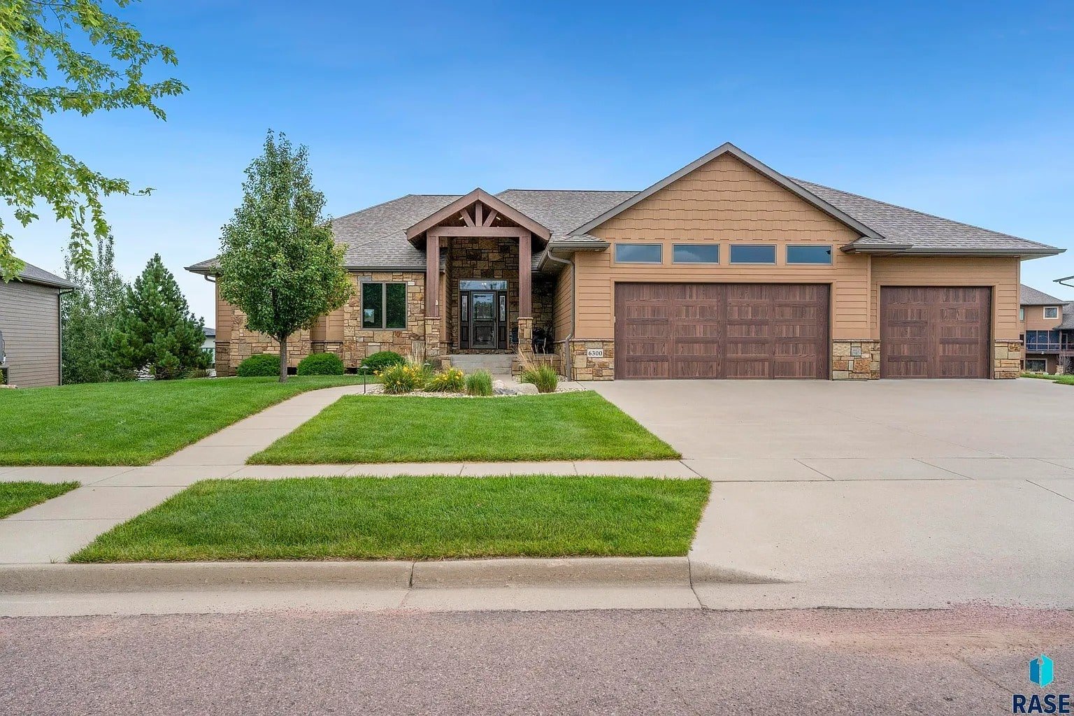 Single-story house with stone accents, three-car garage, and manicured lawn under a clear blue sky.