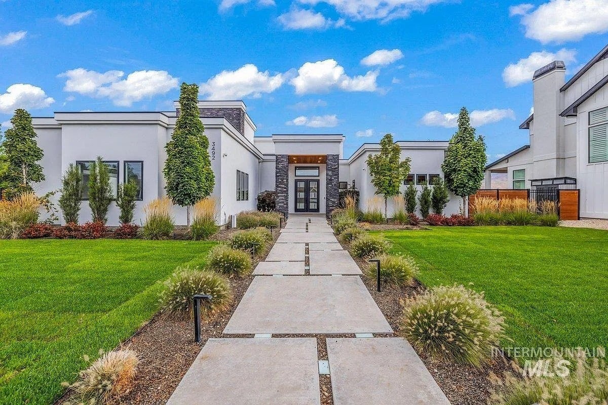 Modern white house with large windows, manicured lawn, and a straight concrete walkway.
