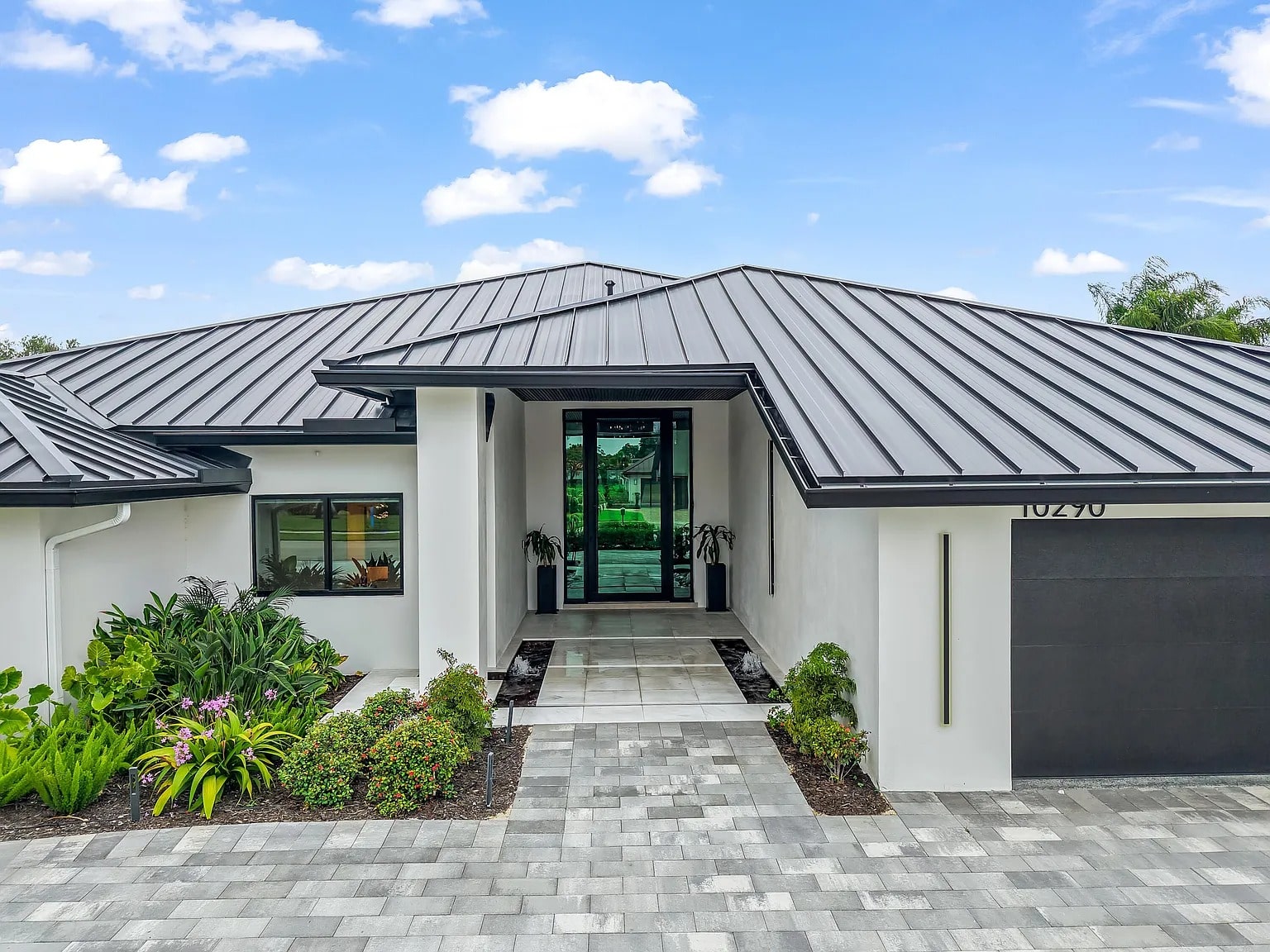 Modern house with a metal roof, large glass entrance, and landscaped front yard.