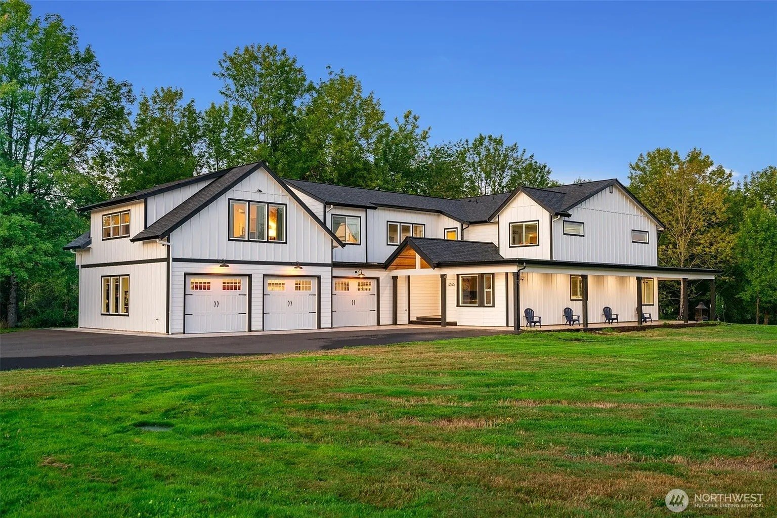 Large modern farmhouse with white siding, black trim, and a spacious lawn, surrounded by trees.