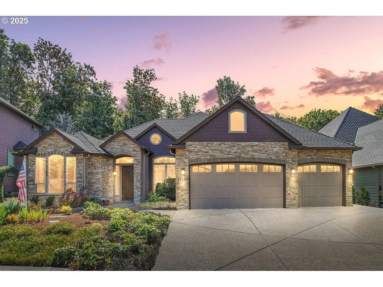 Single-story house with stone facade, three-car garage, and landscaped yard at sunset.