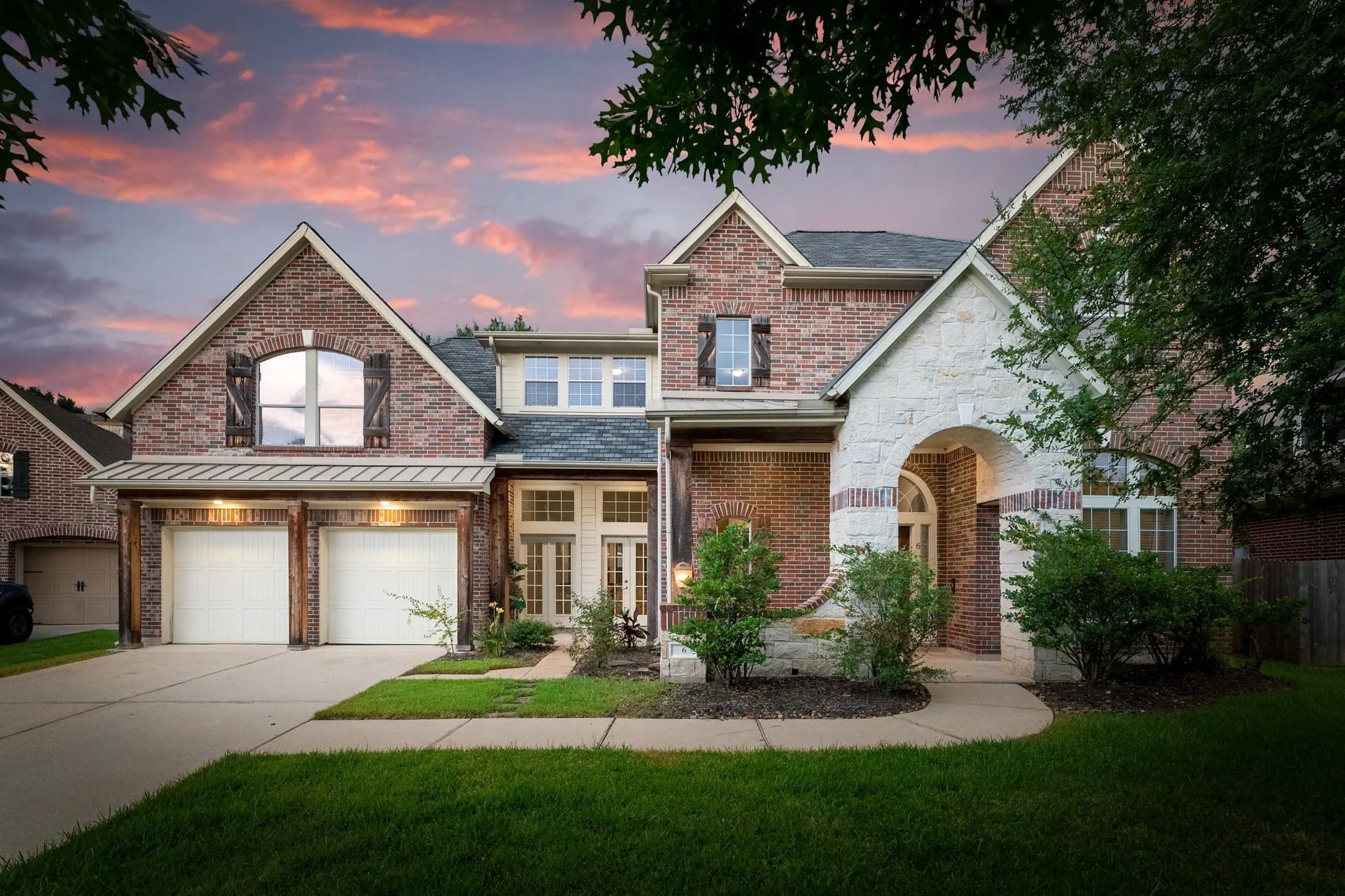 Brick house with a two-car garage and arched entrance, set against a sunset sky.