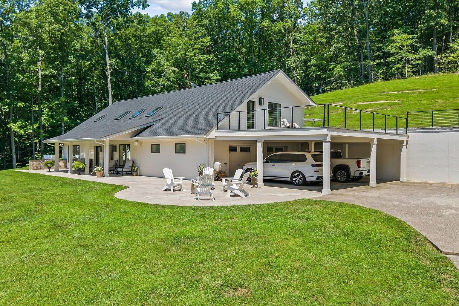 Modern house with a carport, patio furniture, and surrounded by lush greenery.