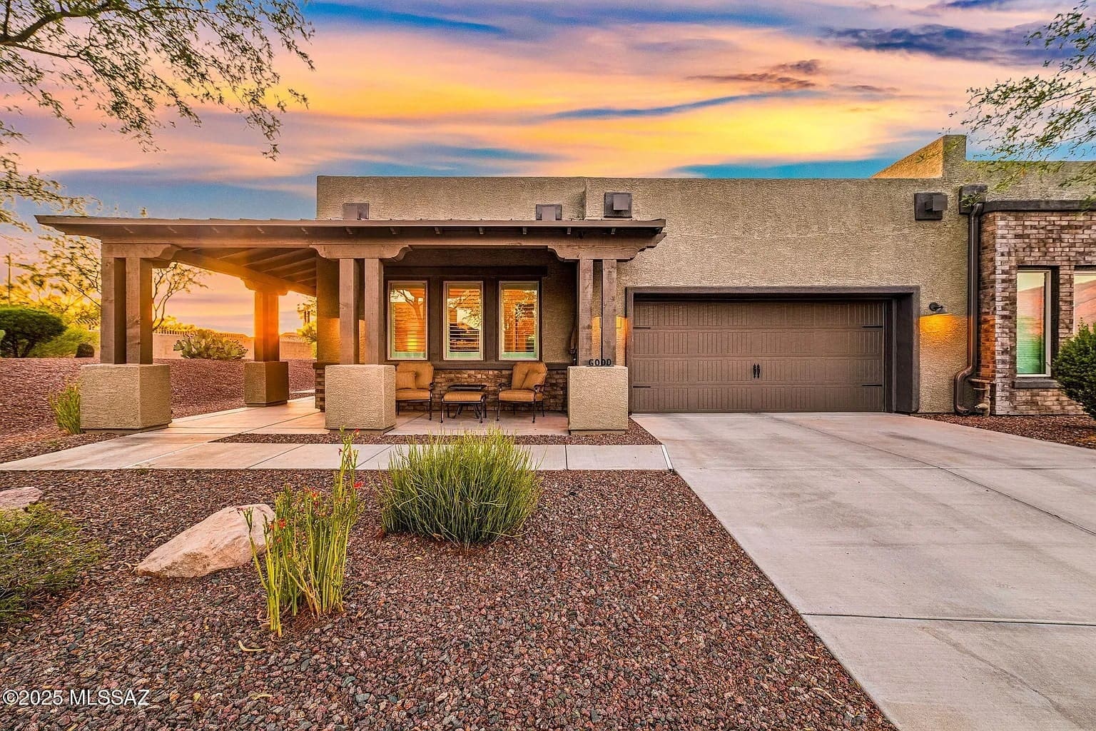 Modern house with a covered patio, garage, and desert landscaping at sunset.