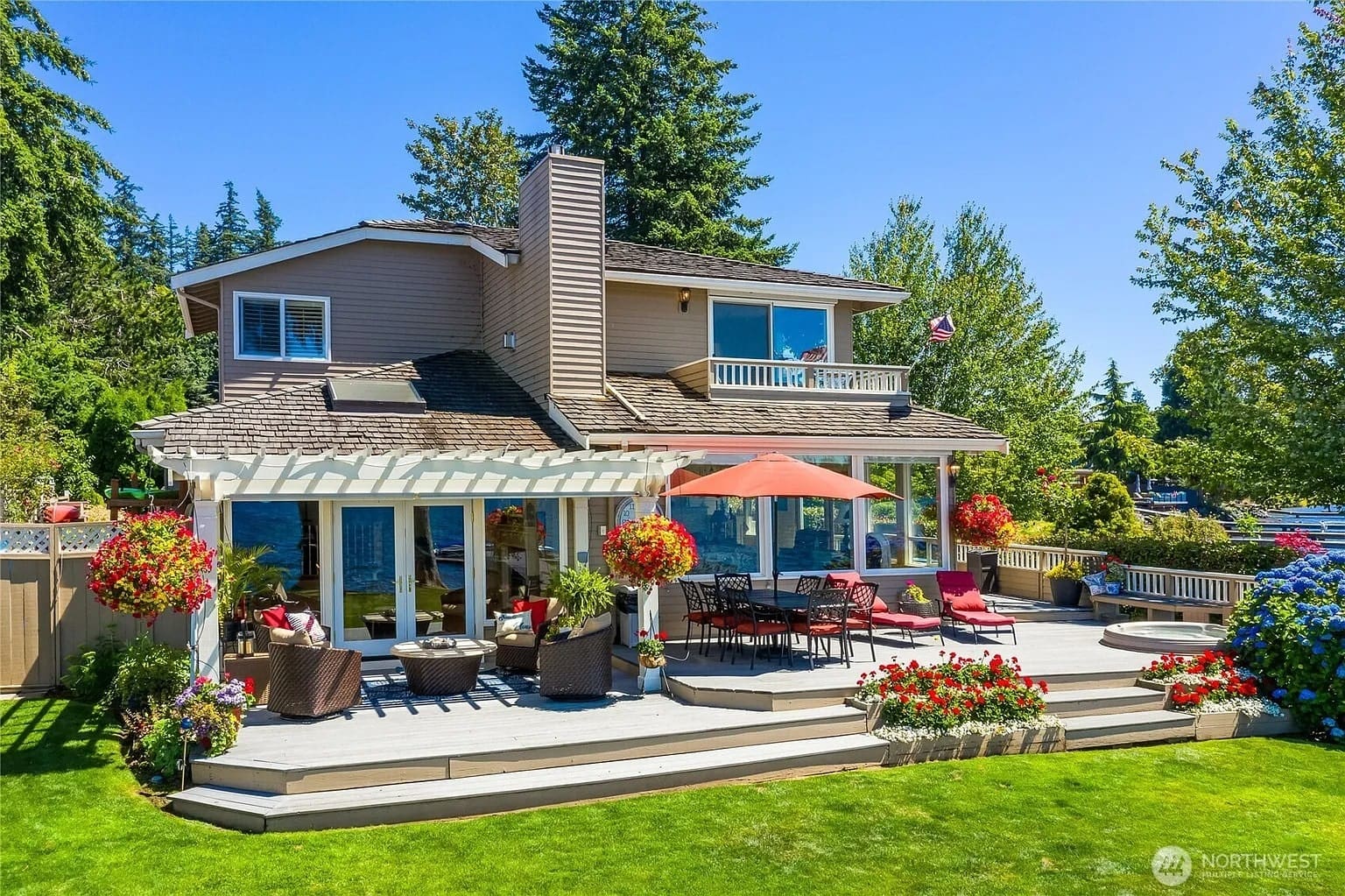 Two-story house with a large deck, outdoor seating, and vibrant flower arrangements.