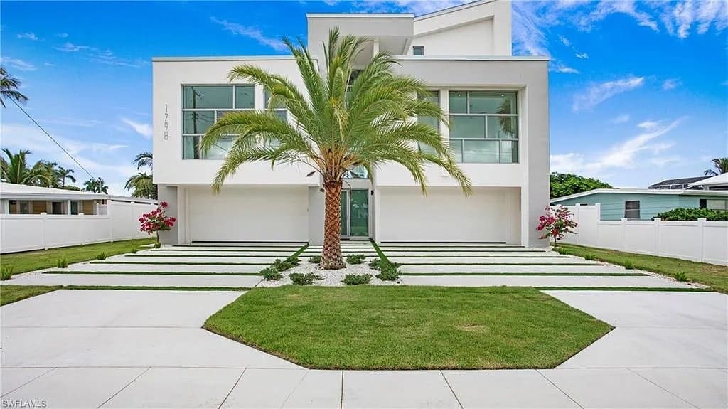 Modern white house with large windows, palm tree in front, and a neatly landscaped yard.