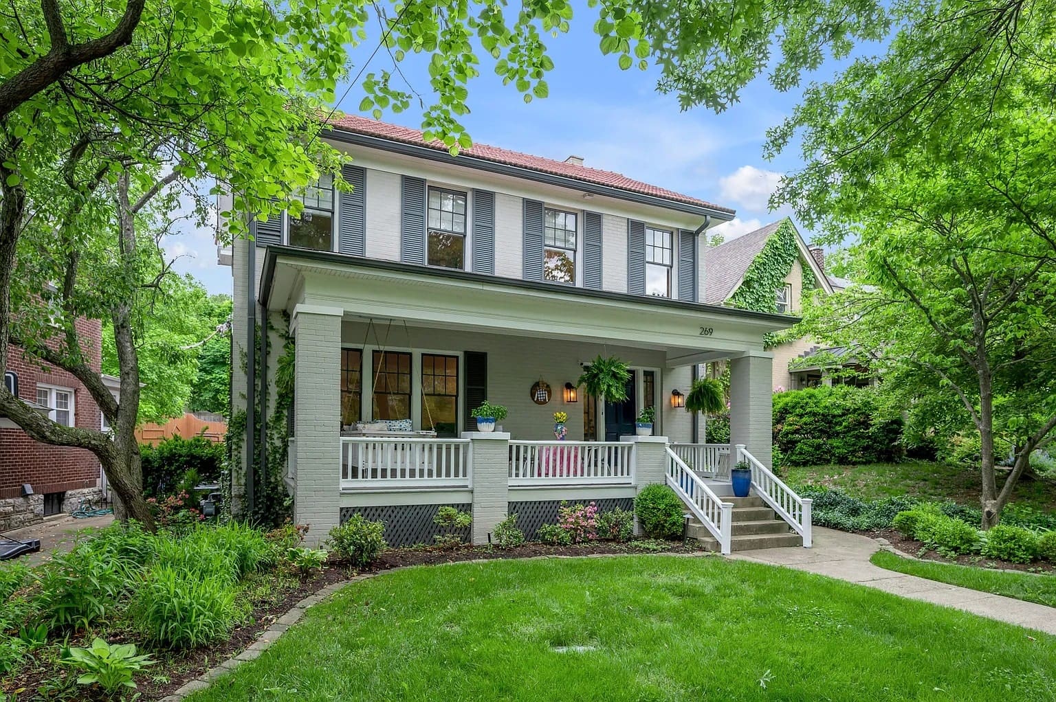Two-story house with a porch, surrounded by lush greenery and a well-kept lawn.
