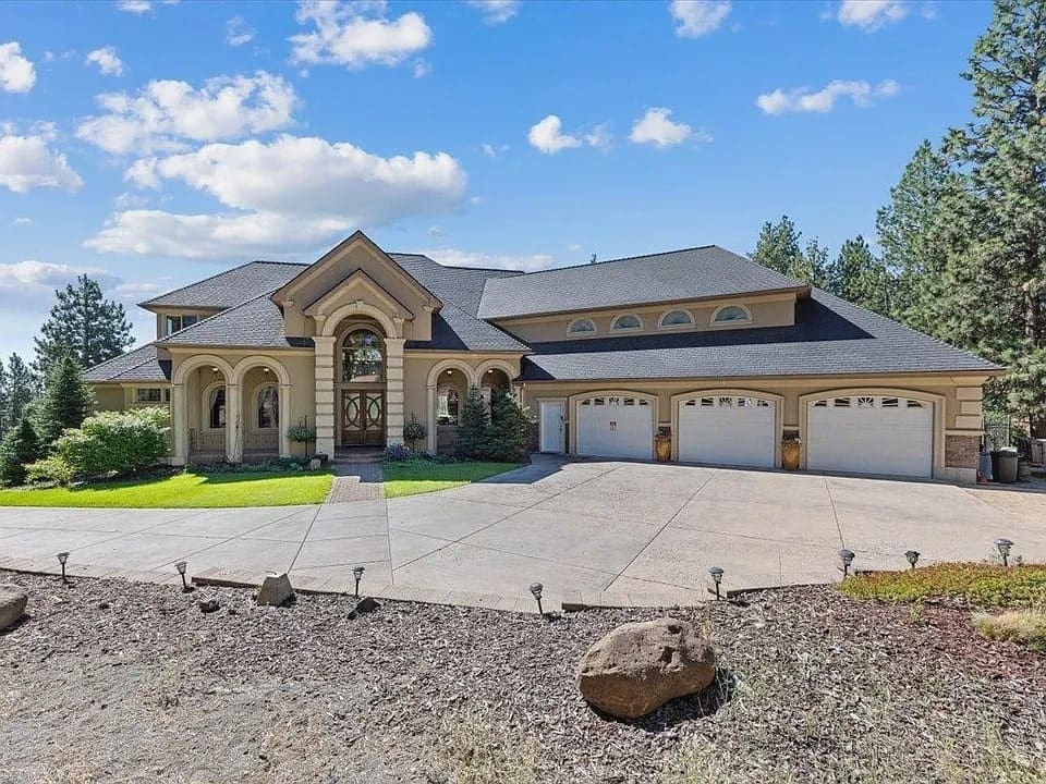 Large, elegant house with arched windows, three-car garage, and landscaped yard under a blue sky.