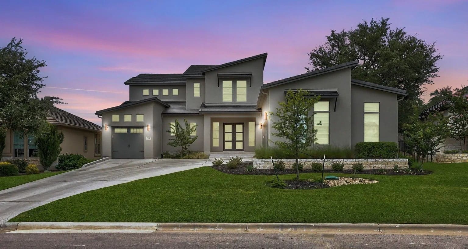Modern two-story house with large windows, sloped roof, and well-maintained lawn at sunset.