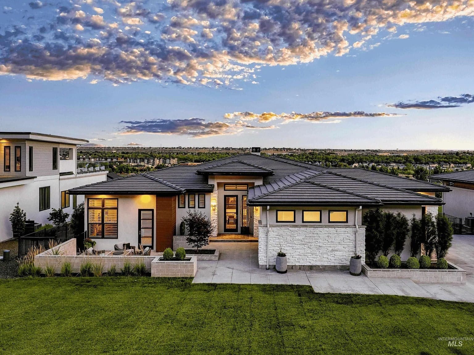 Modern single-story house with large windows, surrounded by a manicured lawn and dramatic sky.