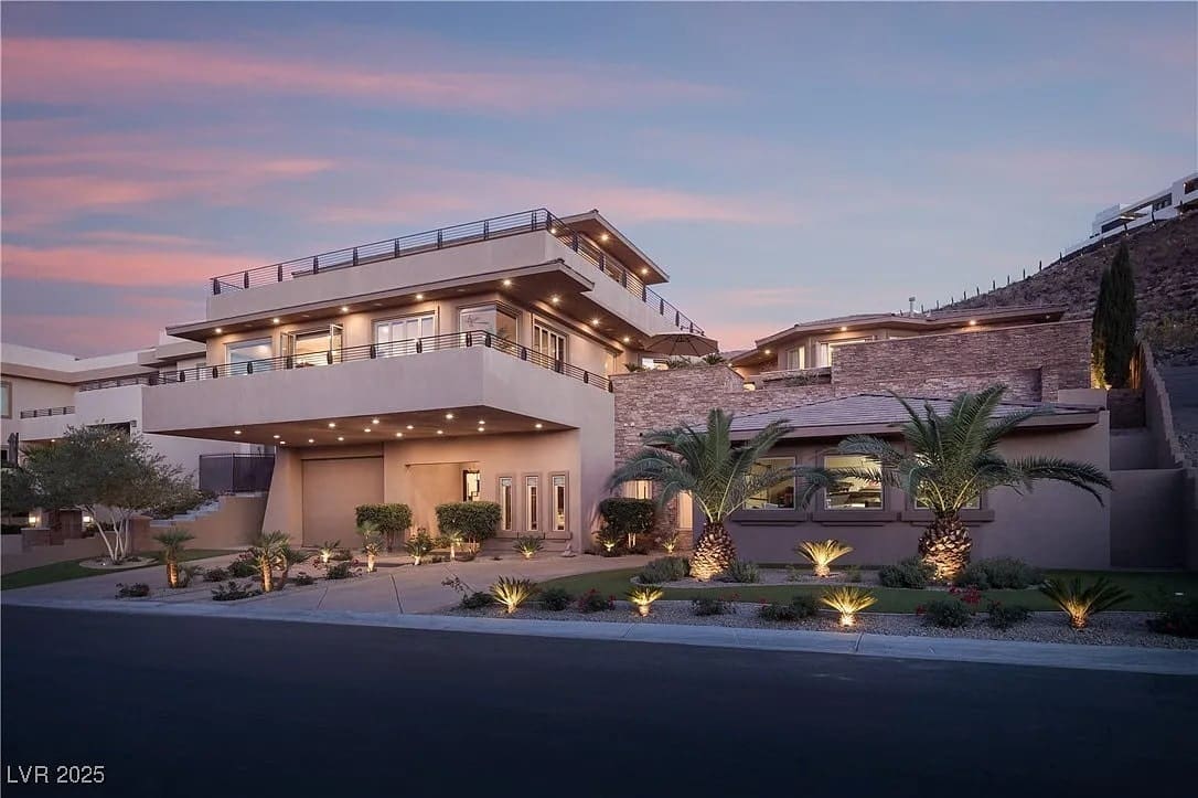 Modern multi-story house with large balconies, palm trees, and evening lighting under a pink sky.