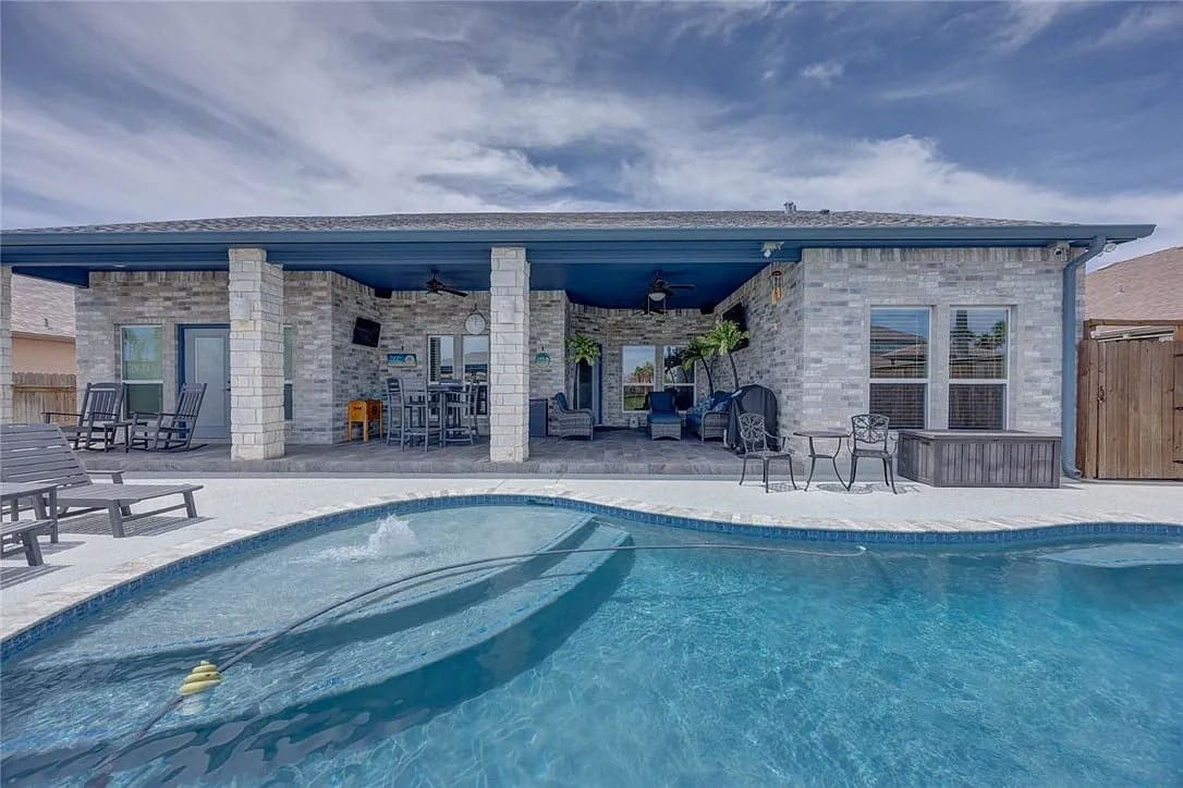 Backyard with a swimming pool, patio seating, and a covered outdoor area under a cloudy sky.