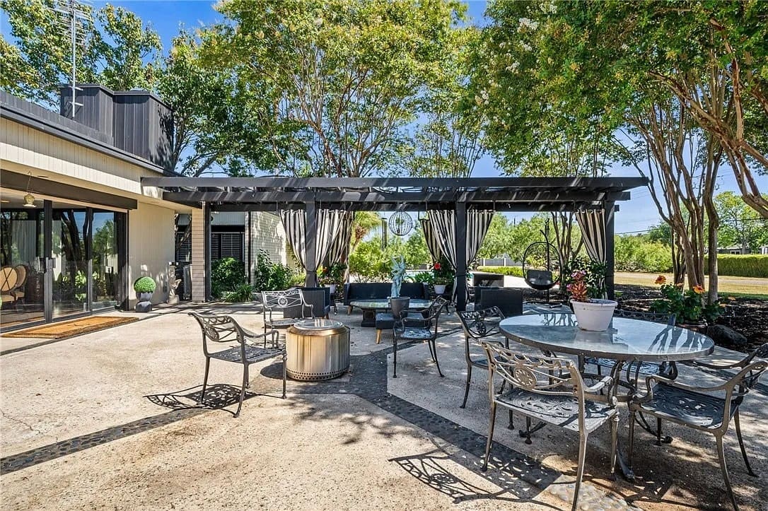 Outdoor patio with metal furniture, pergola, and trees providing shade.