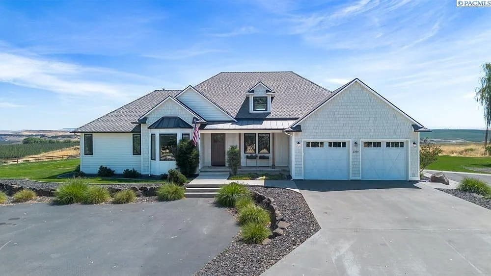 Single-story white house with a two-car garage, surrounded by a spacious driveway and open landscape.