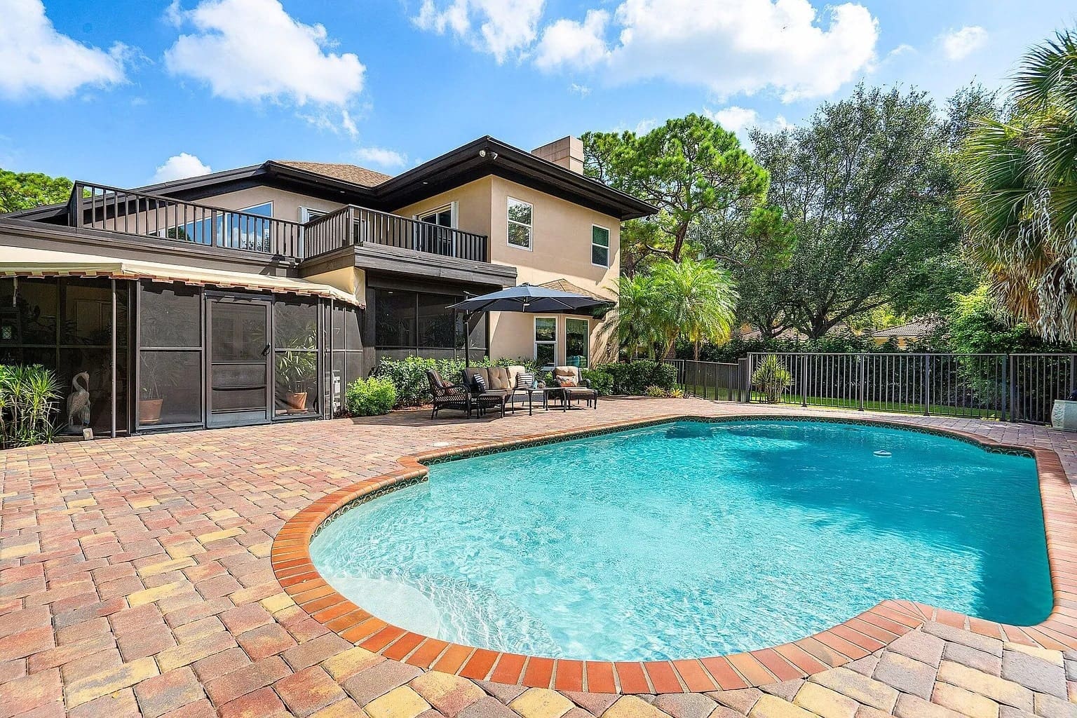 Backyard with a swimming pool, patio furniture, and a two-story house surrounded by trees.