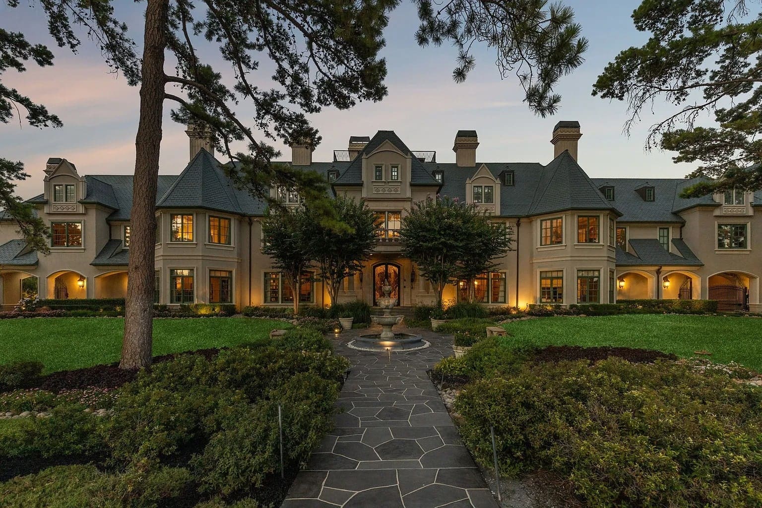 Large, elegant mansion with multiple chimneys, surrounded by trees and a well-manicured lawn.