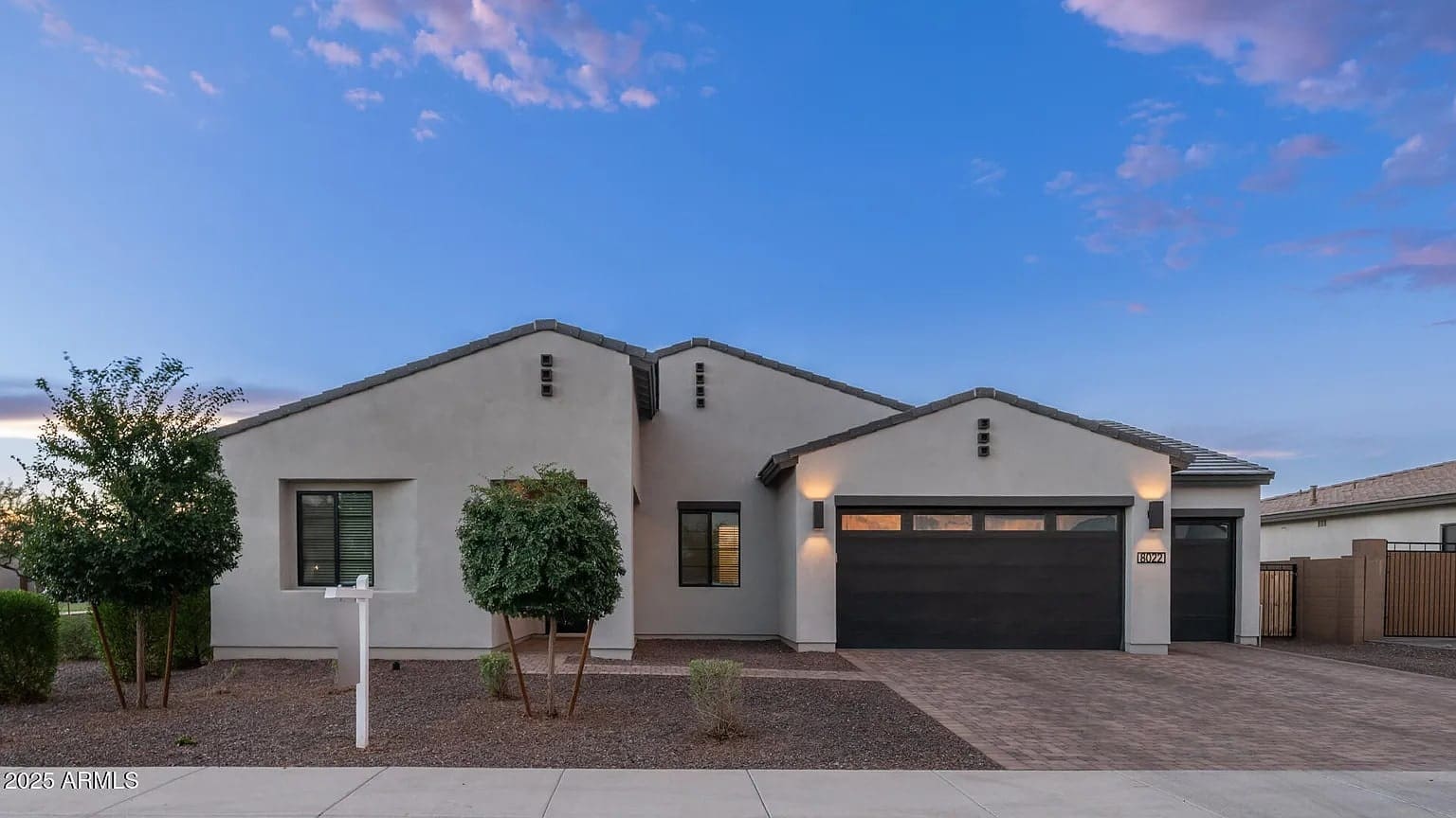 Single-story modern house with a two-car garage and a small front yard under a blue sky.