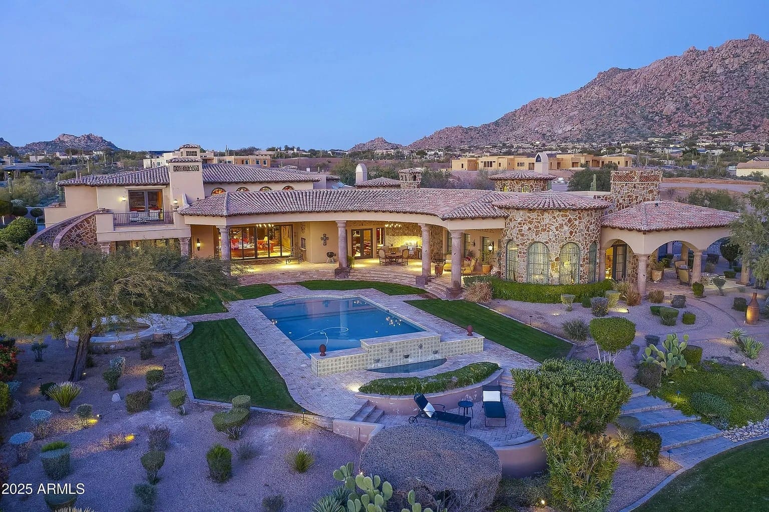 Luxurious villa with a pool, surrounded by landscaped gardens and desert mountains in the background.