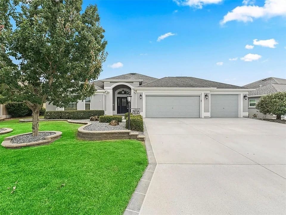 Single-story house with a three-car garage, manicured lawn, and a tree in the front yard.